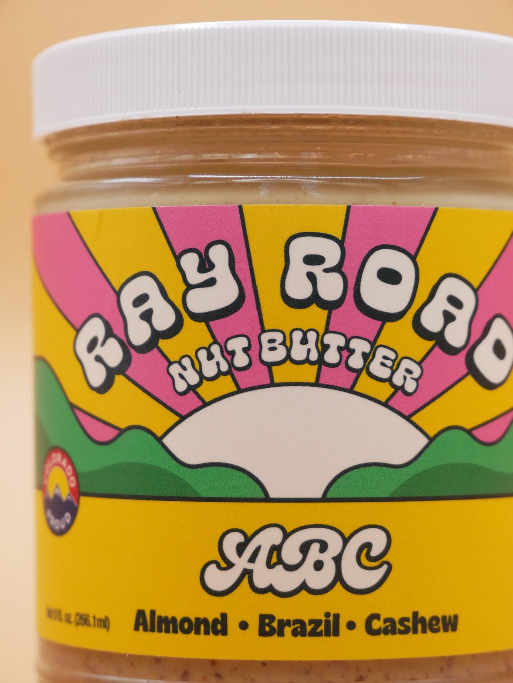 A close-up of a jar of Ray Road Nut Butter ABC Almond Brazil Cashew nut butter with a colorful retro label and a white lid.