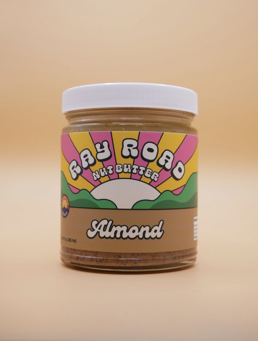 jar of ray road nut butter almond butter, brown label, rainbow logo, peach background