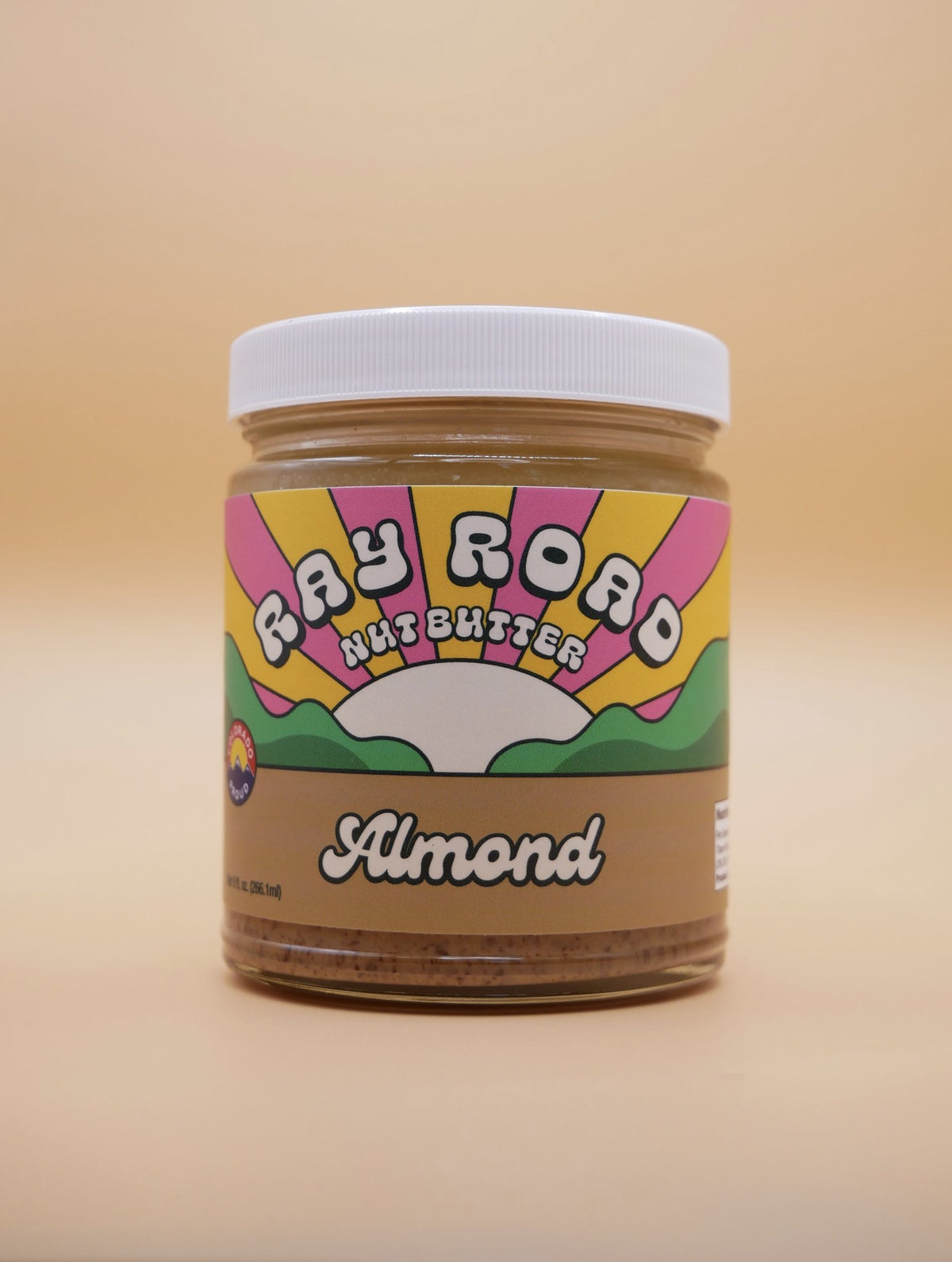 jar of ray road nut butter almond butter, brown label, rainbow logo, peach background