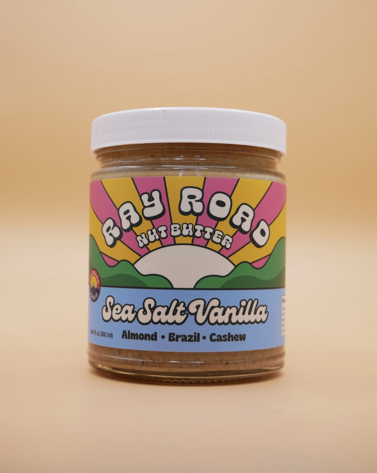 jar of ray road nut butter, sea salt vanilla flavor. ray road rainbow logo with blue. peach background
