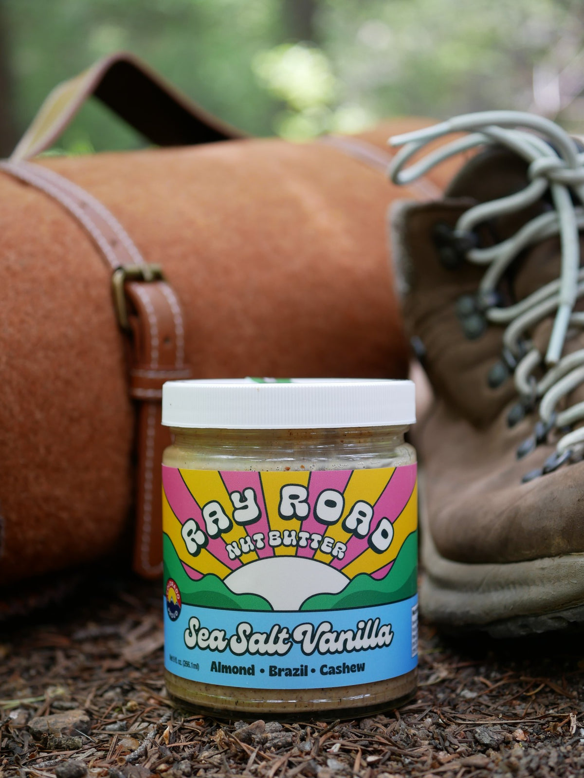 jar of ray road nut butter sea salt vanilla on a ground of twigs, in front of hiking boots and pack