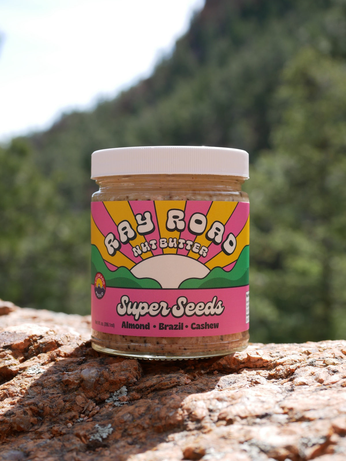 A jar of Ray Road nut butter resting on a rock with a mountain valley behind it